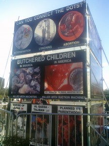 A billboard of a bloody fetus sits outside the "Free Assembly Area"